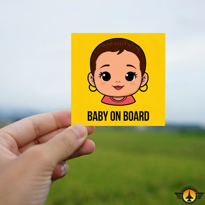 Hand holding a 'Baby on Board' sticker with a bold cartoon baby face on a yellow background.