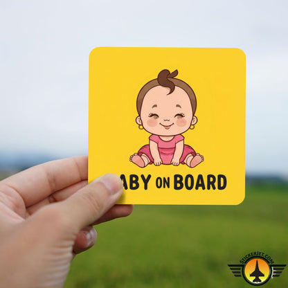 Hand holding a yellow card with a baby illustration and Baby On Board Sticker – Cartoon Baby Girl Design against a blurred natural background.
